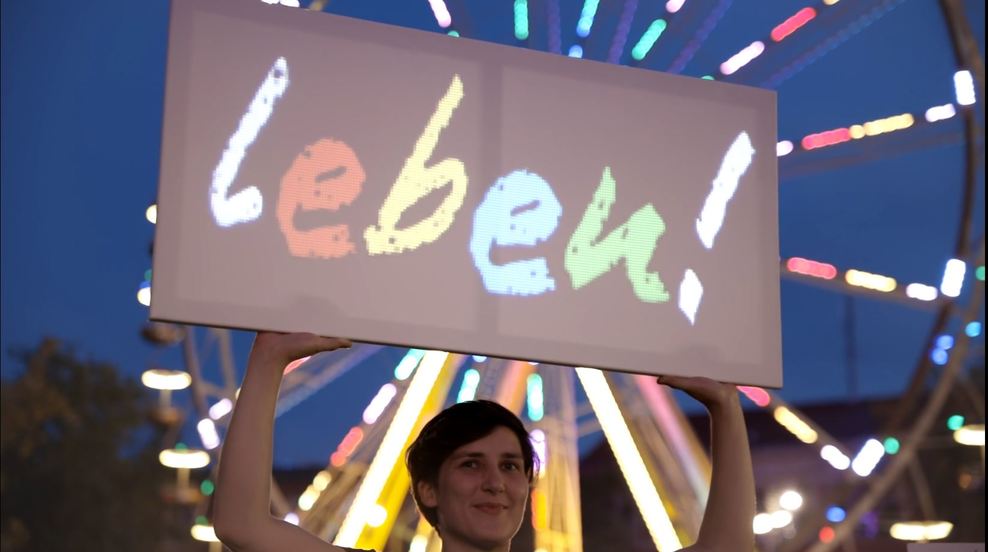 Frau mit Schild mit bunter Aufschrift "Leben!"